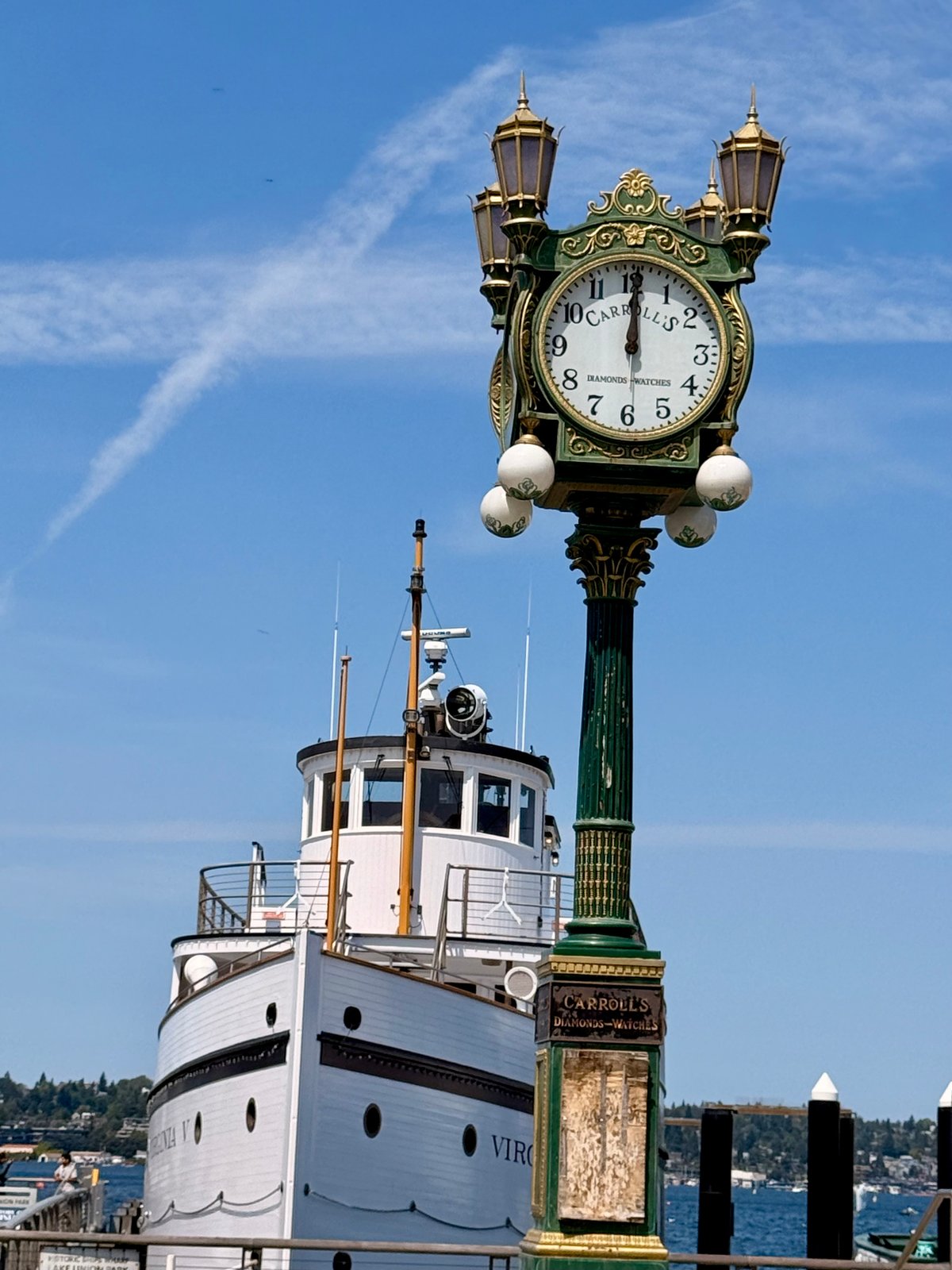 A vintage street clock, Carroll's Diamonds-Watches, stands in front of a white boat, Virginia V, under a blue sky.
